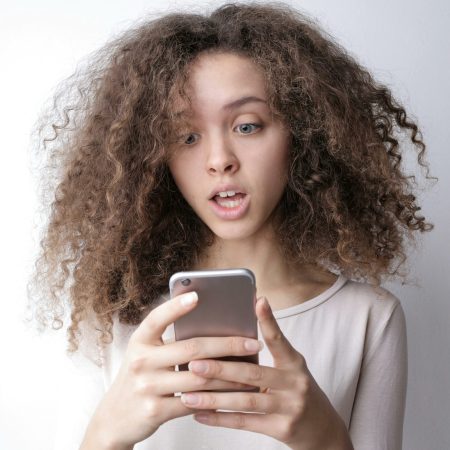 une femme devant son smartphone représentant les différentes arnaques par SMS